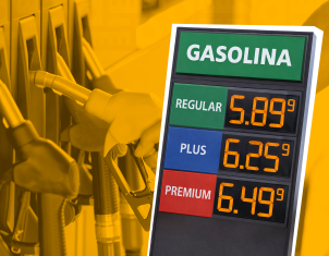 Un letrero que muestra los precios de gasolina (Regular, Plus, Premium) junto a las mangueras de una estación de servicio en tono amarillento.