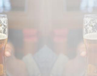 Gentleman with a beard holding a glass of beer toasting with another person